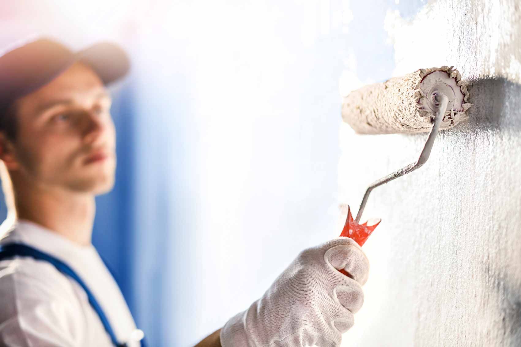 A painter is rolling white paint onto an interior wall.