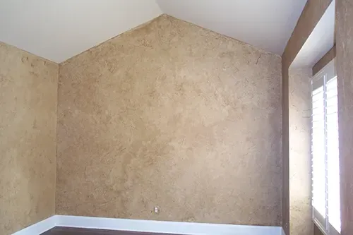 Beige textured walls in a room with a white ceiling, dark floor, and shuttered window. Empty tan bedroom with white trim and a tall window on the right
