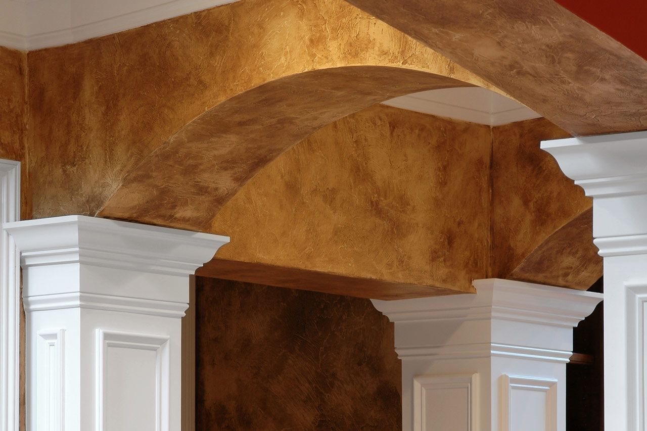 Our goal is to create a finish that looks handcrafted, timeless, and uniquely yours. White columns beneath a tan stucco archway in an interior space