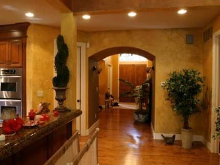 Interior of a home with arched doorways, warm yellow walls, wood floors, and potted plants. Warm-toned home hallway with polished wood floors, granite counter, and decorative plants leading to an archway