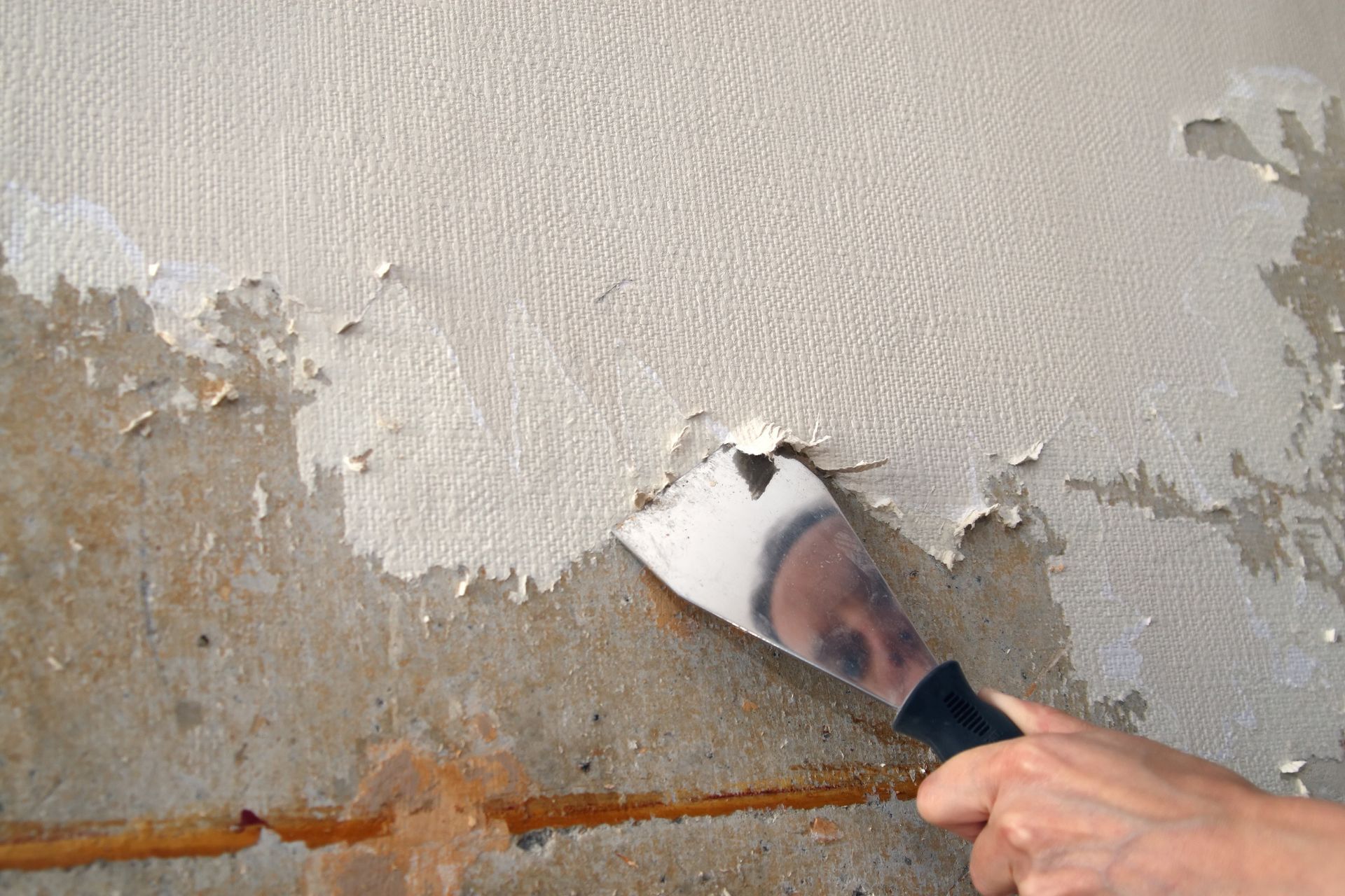 Hand scraping peeling paint from a beige wall with a putty knife