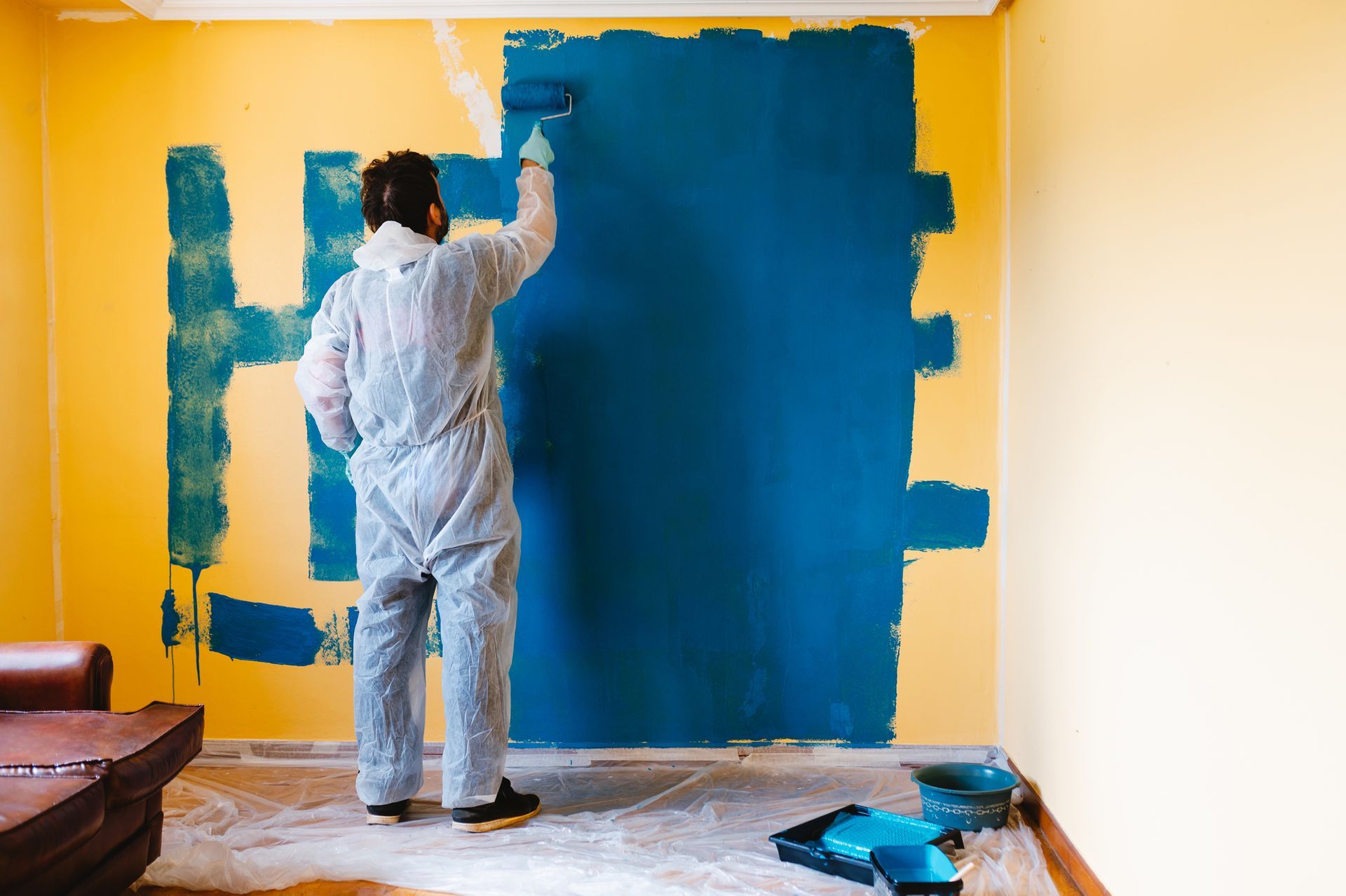 Person painting a wall blue over a yellow background in a room