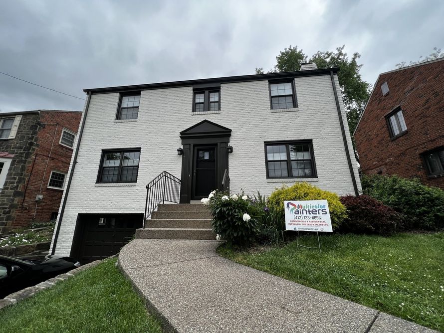 White two-story house with black trim, curved walkway, and a real estate sign on the front lawn