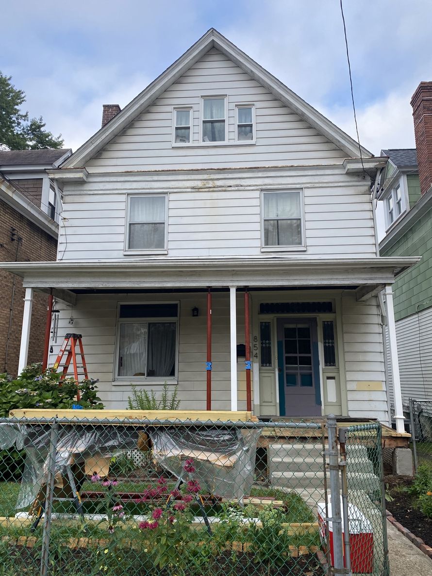 Weathered white two-story house with a front porch and steps, seen from the street