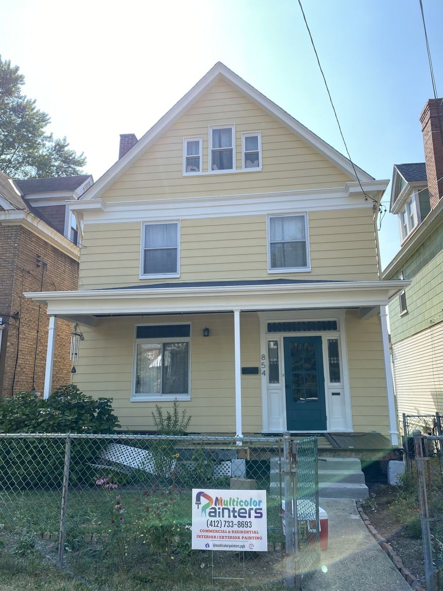 Yellow two-story house with front porch and a real estate sign in the yard