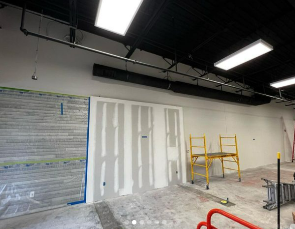 Construction site interior with drywall, scaffolding, and pipes. White walls, black ceiling.