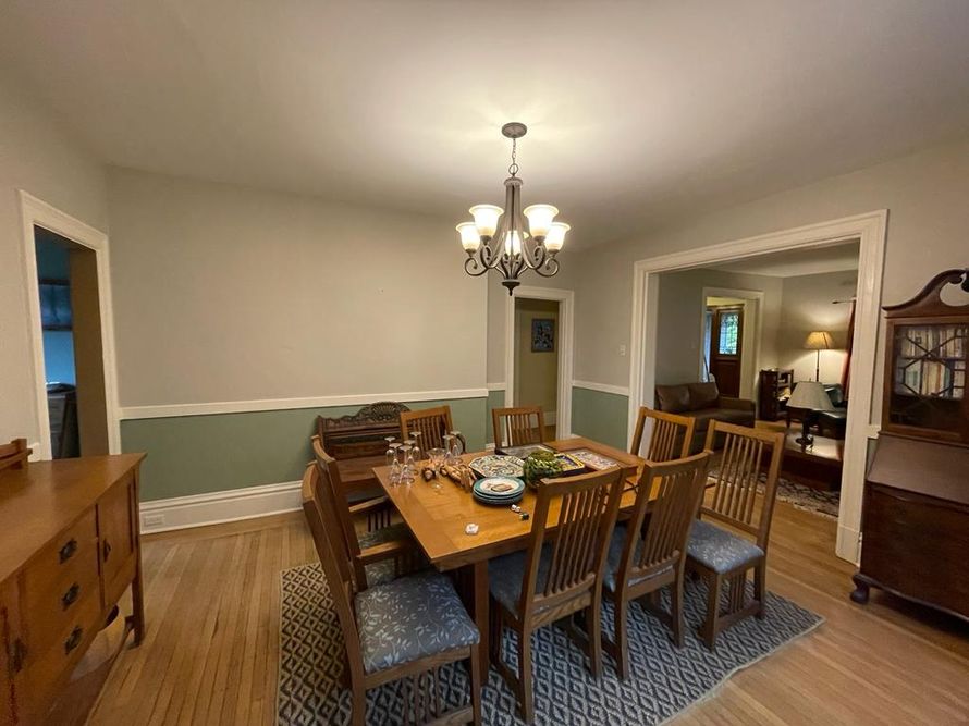 Dining room with wooden table and chairs, chandelier, and green-and-white walls.