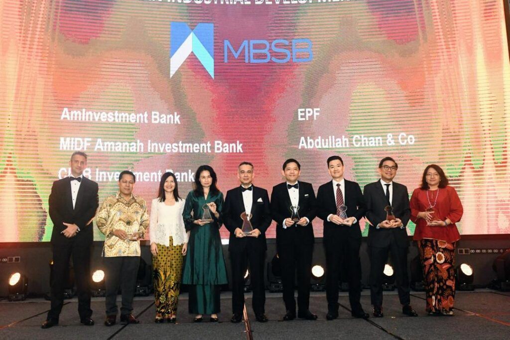 Abdullah Chan & Co with awards on a stage in front of a screen with the MBSS logo.