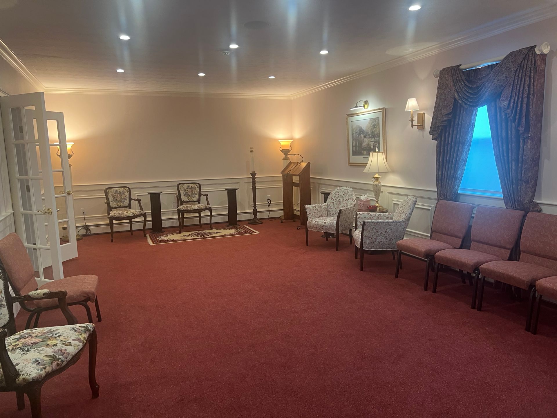 Empty meeting room with red carpet, rows of chairs, and white walls lit by warm ceiling lights