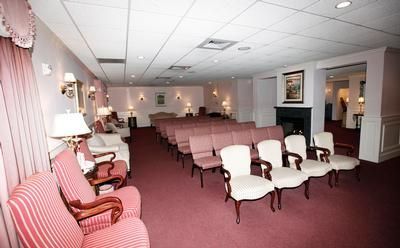 Empty waiting room with rows of chairs, pink carpet, lamps, and framed wall art
