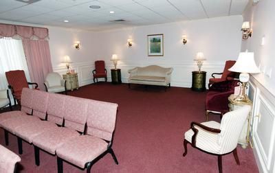 Empty waiting room with pink chairs, maroon carpet, cream sofas, and wall lamps