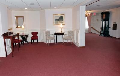 Spacious red-carpeted lounge with white walls, small tables and chairs, and a stairway on the right.