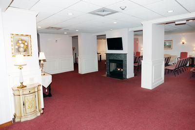 Spacious carpeted lounge with white walls, fireplace, lamps, and seating area in the background