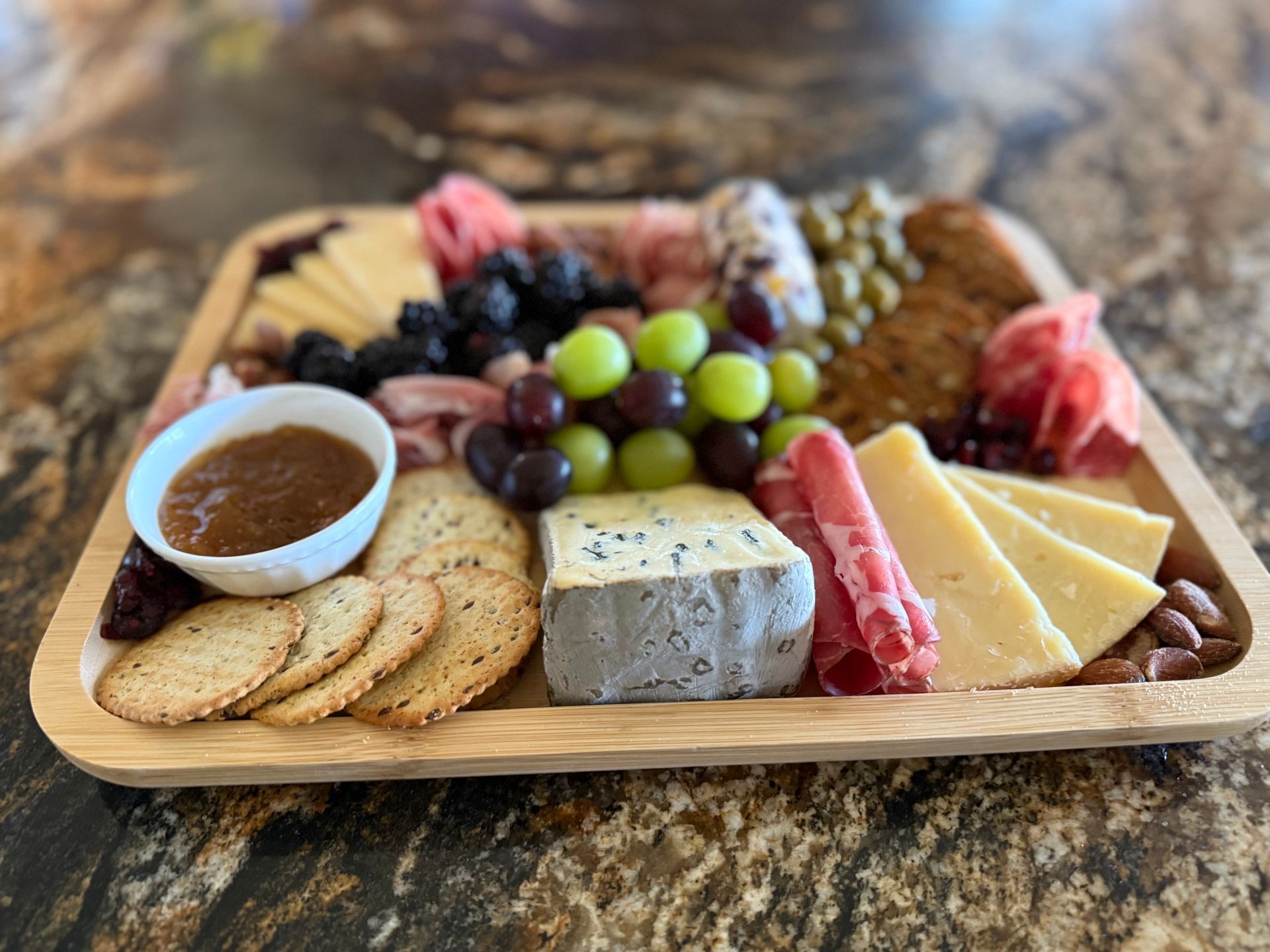 Charcuterie board with grapes, cheese, crackers, and meat, arranged on a wooden tray.