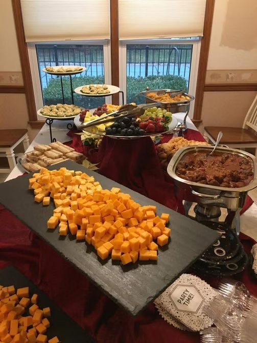Buffet table with cheese cubes, appetizers, fruit, and a dish of food.