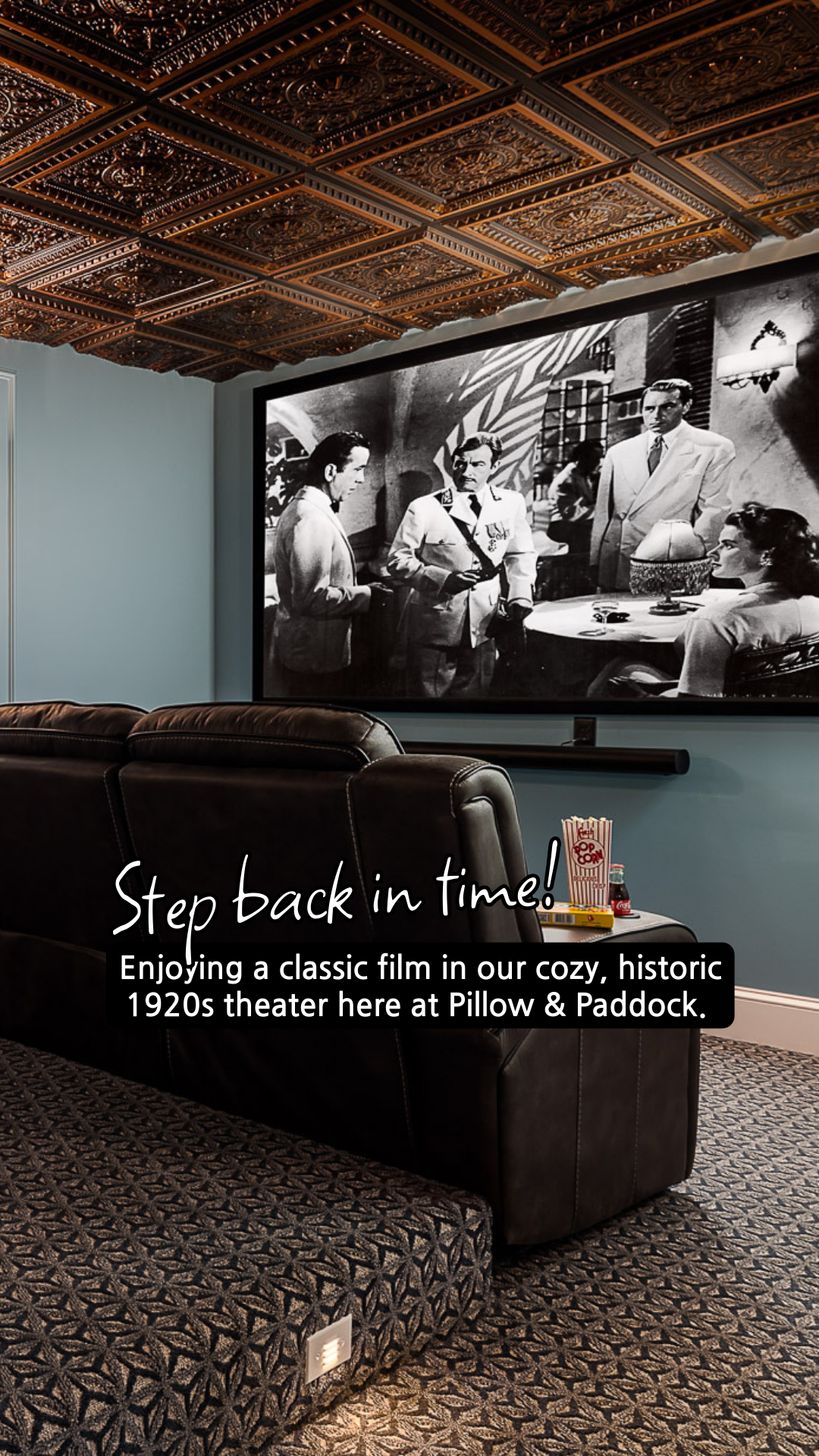 Movie theater with black leather seating, large screen showing a black and white film, decorative ceiling.