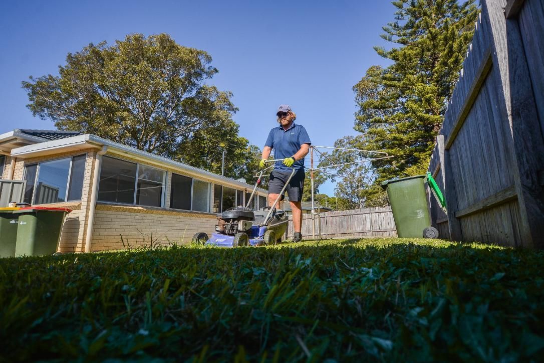 A Man Is Using A Lawn Mower To Cut The Grass In Front Of A House — Tall Orders Port Macquarie In Port Macquarie, NSW