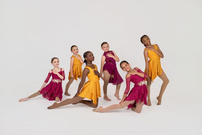 Three young girls in black and pink costumes are dancing