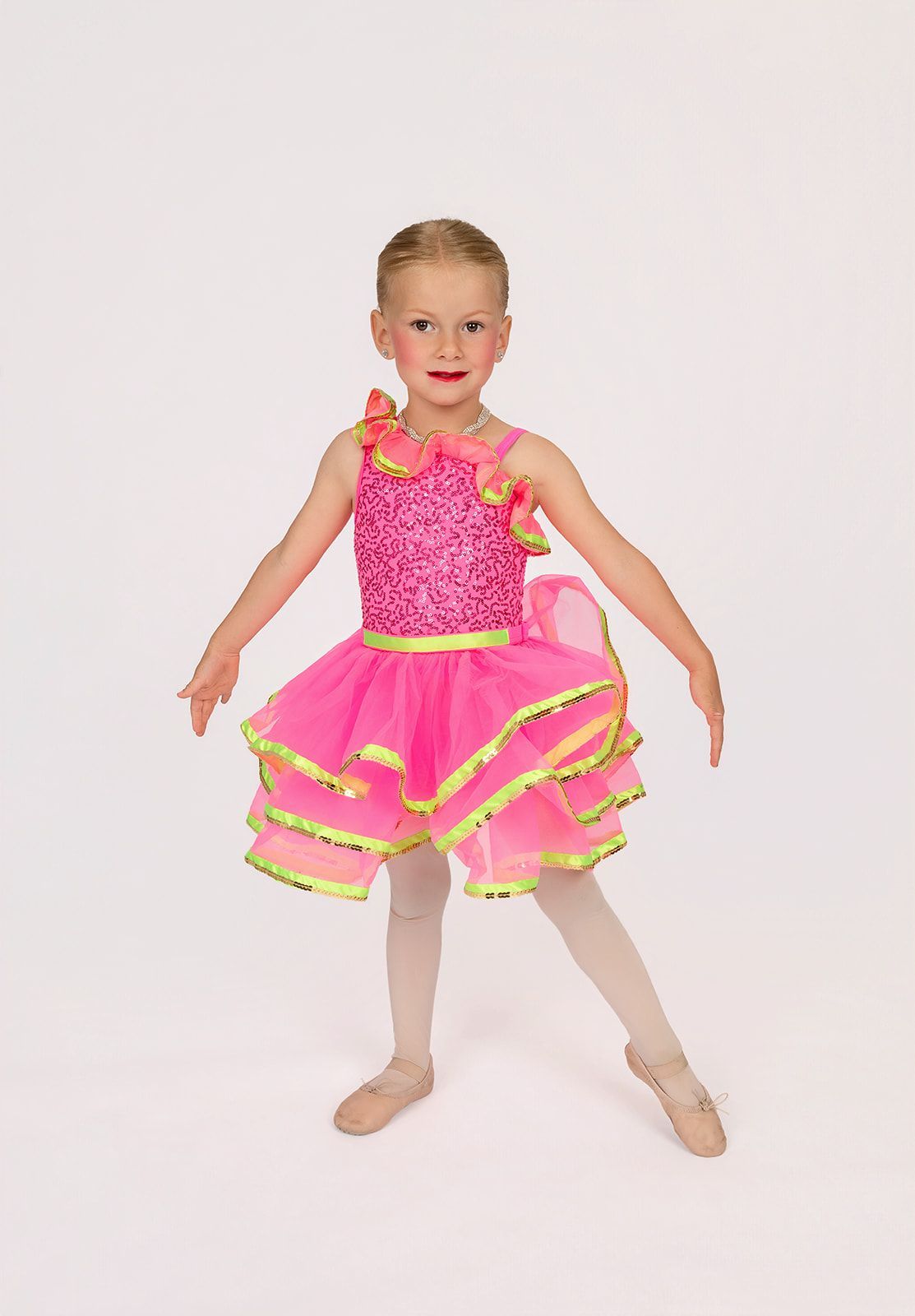 A little girl in a sequined dress is pointing at the camera.