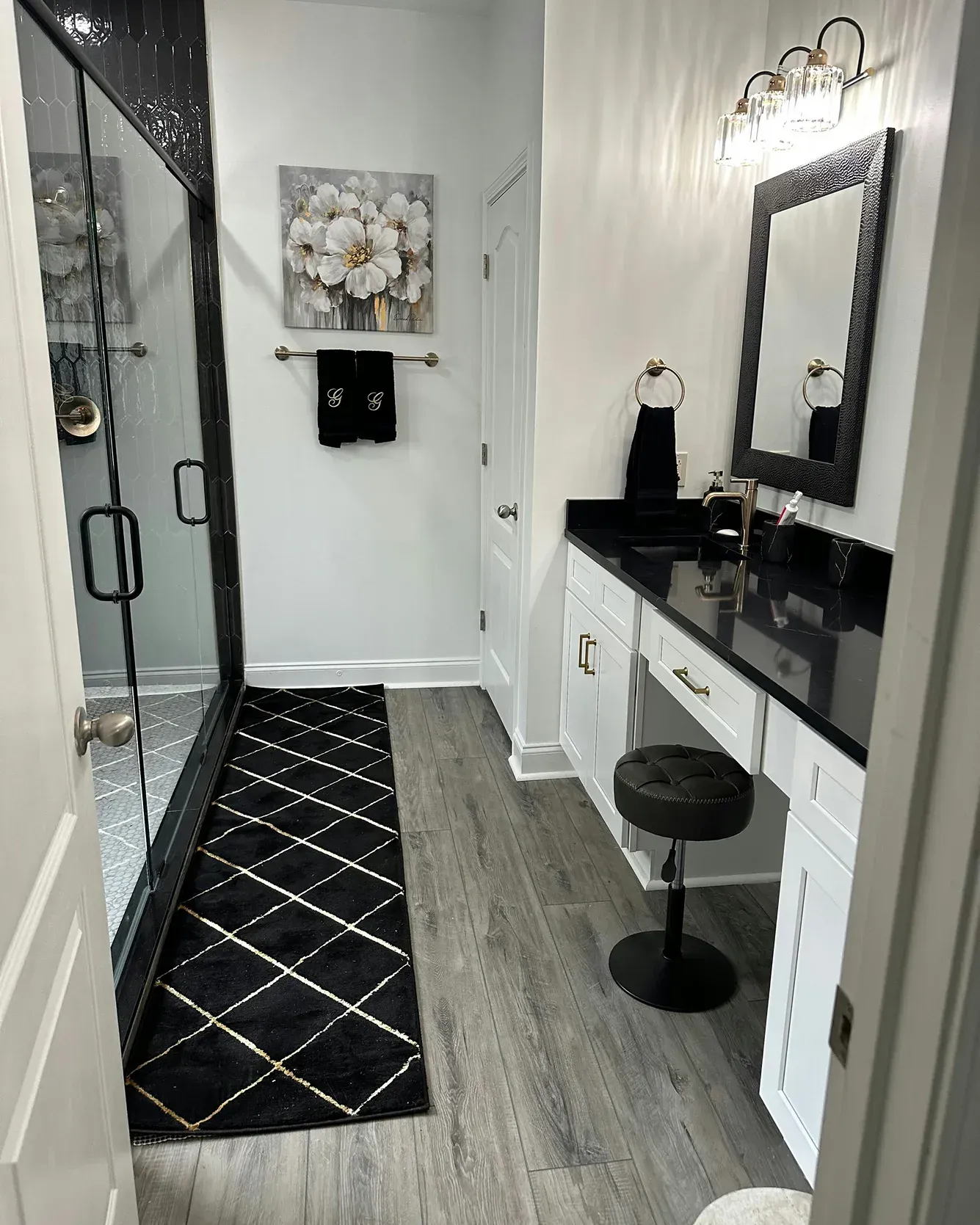Modern bathroom vanity with black-and-white decor, glass shower door, patterned rug, and wall mirror