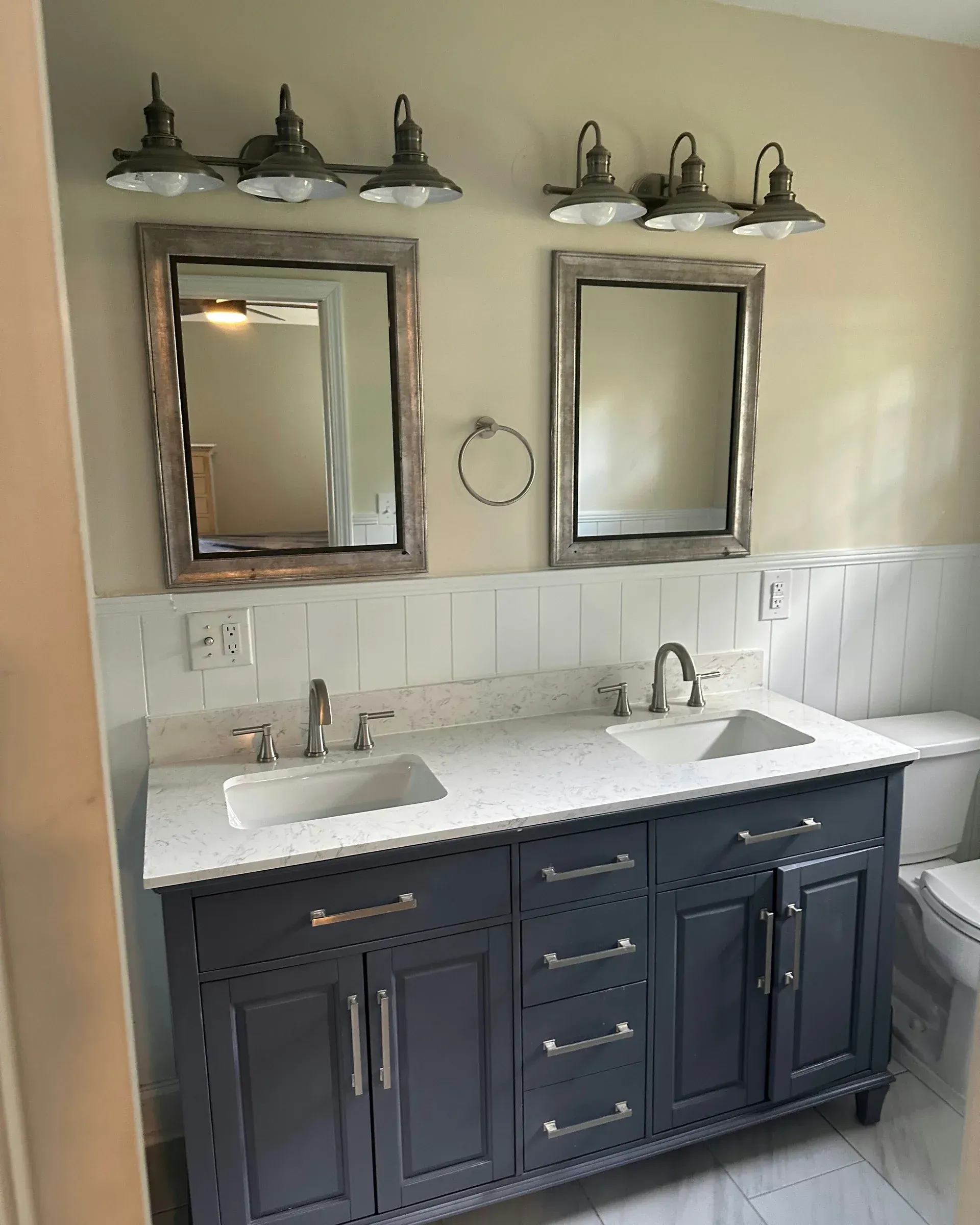 Double vanity bathroom with dark cabinets, white countertop, two mirrors, and wall sconces