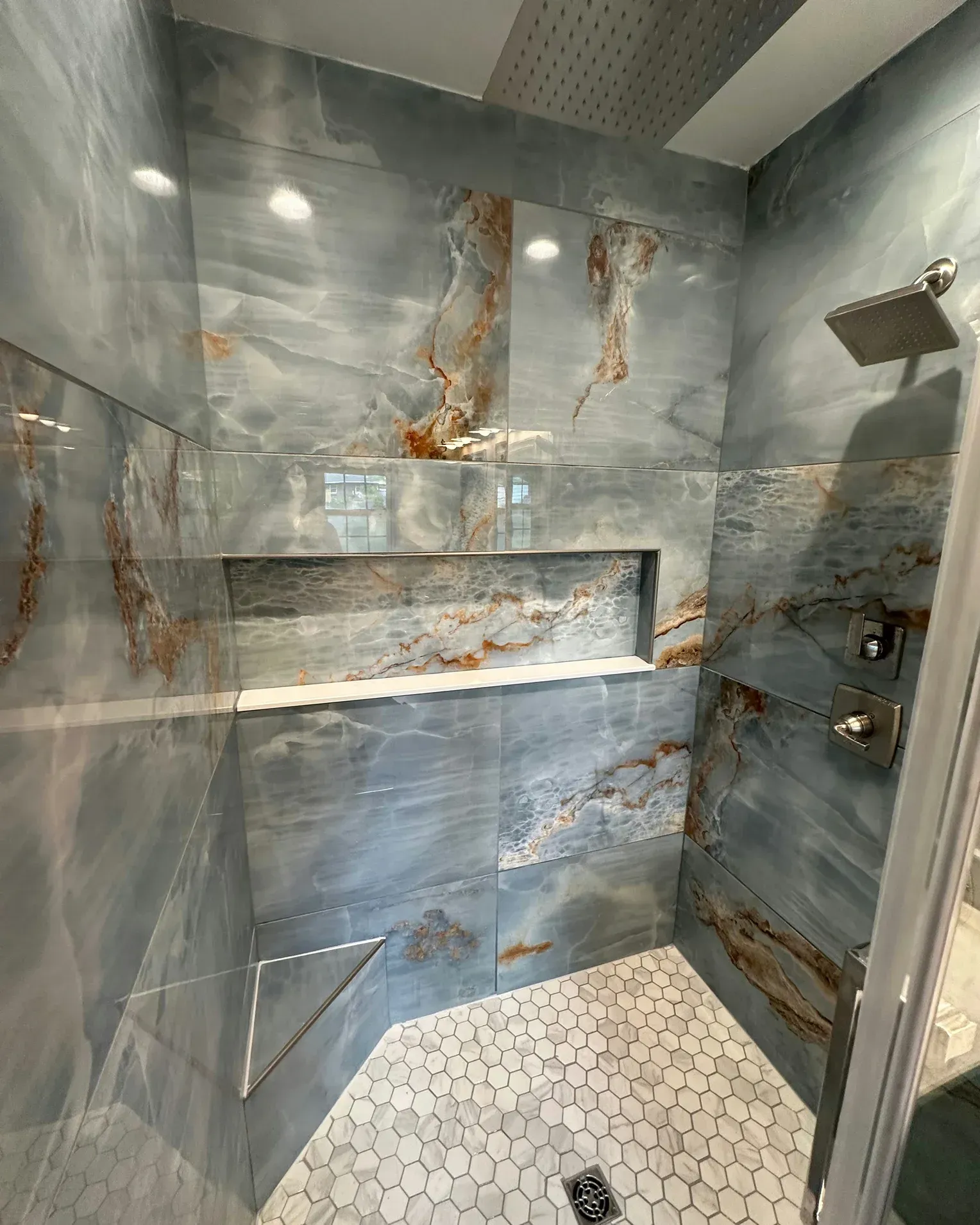 Rusty modern shower with gray marble walls, built-in niches, and hexagon tile floor