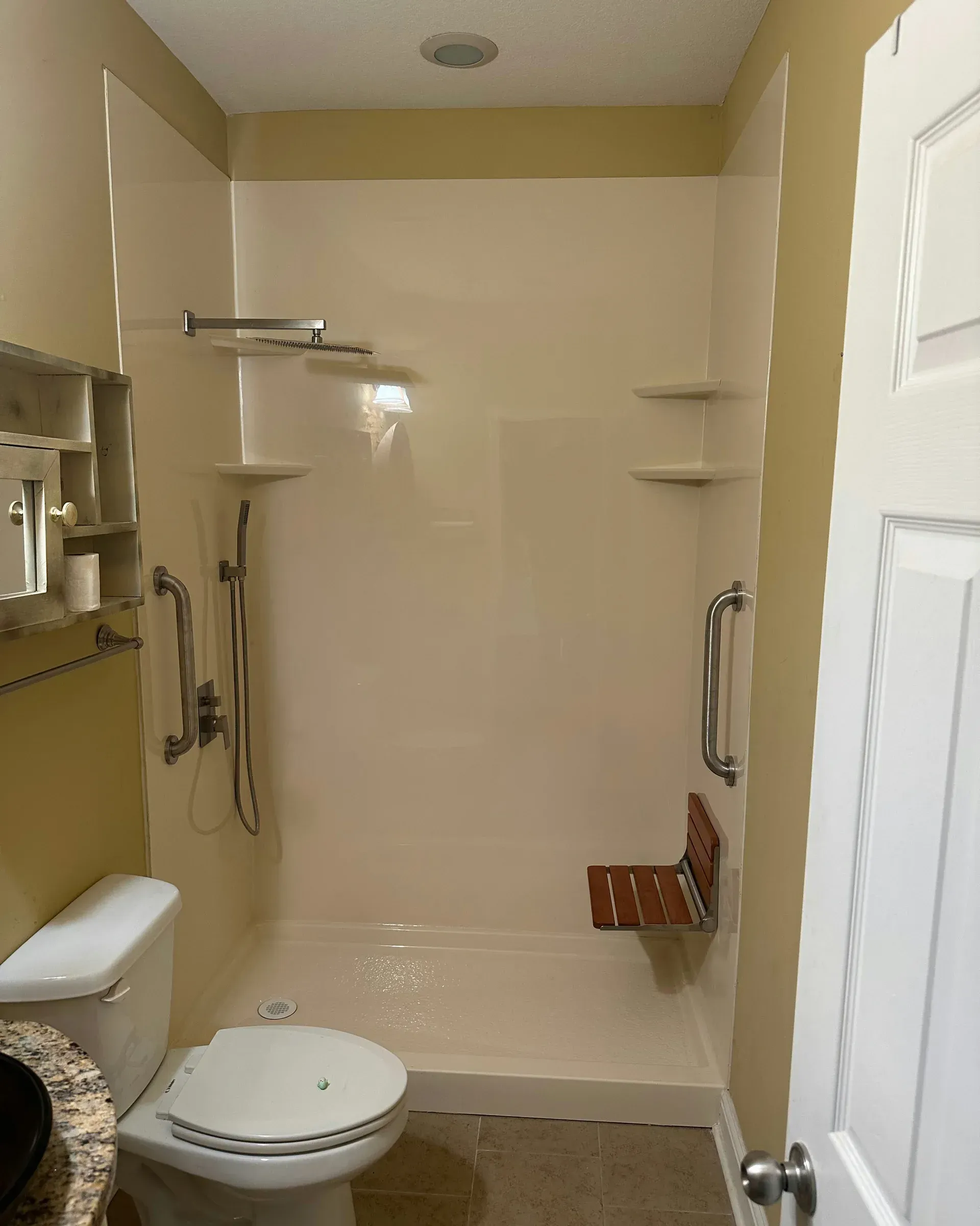 Accessible shower stall with grab bars, built-in shelves, and a fold-down seat in a bathroom
