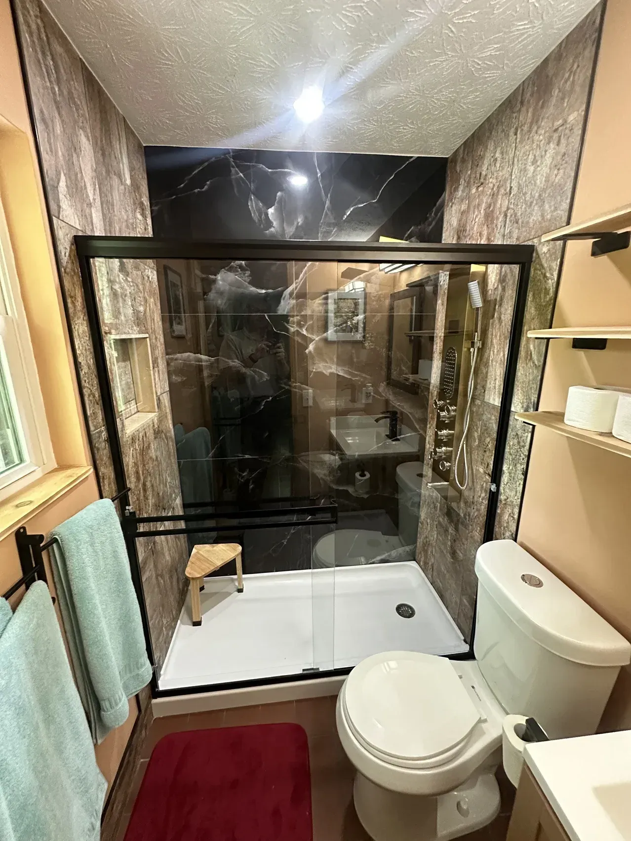 Small bathroom with shower enclosure, toilet, sink, red bath mat, and turquoise towels.