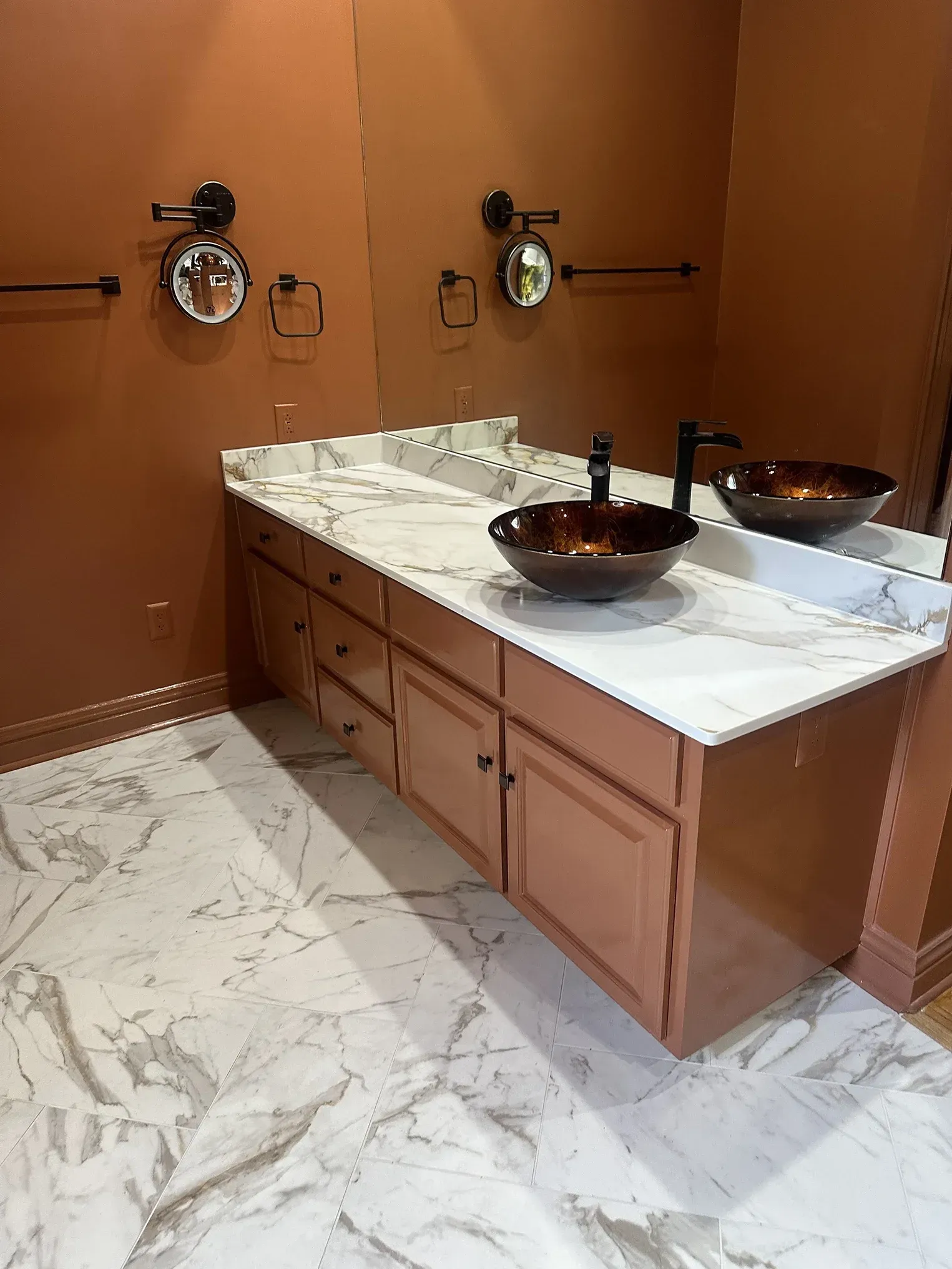 Modern bathroom vanity with marble countertop, copper sinks, and bronze wall-mounted mirrors