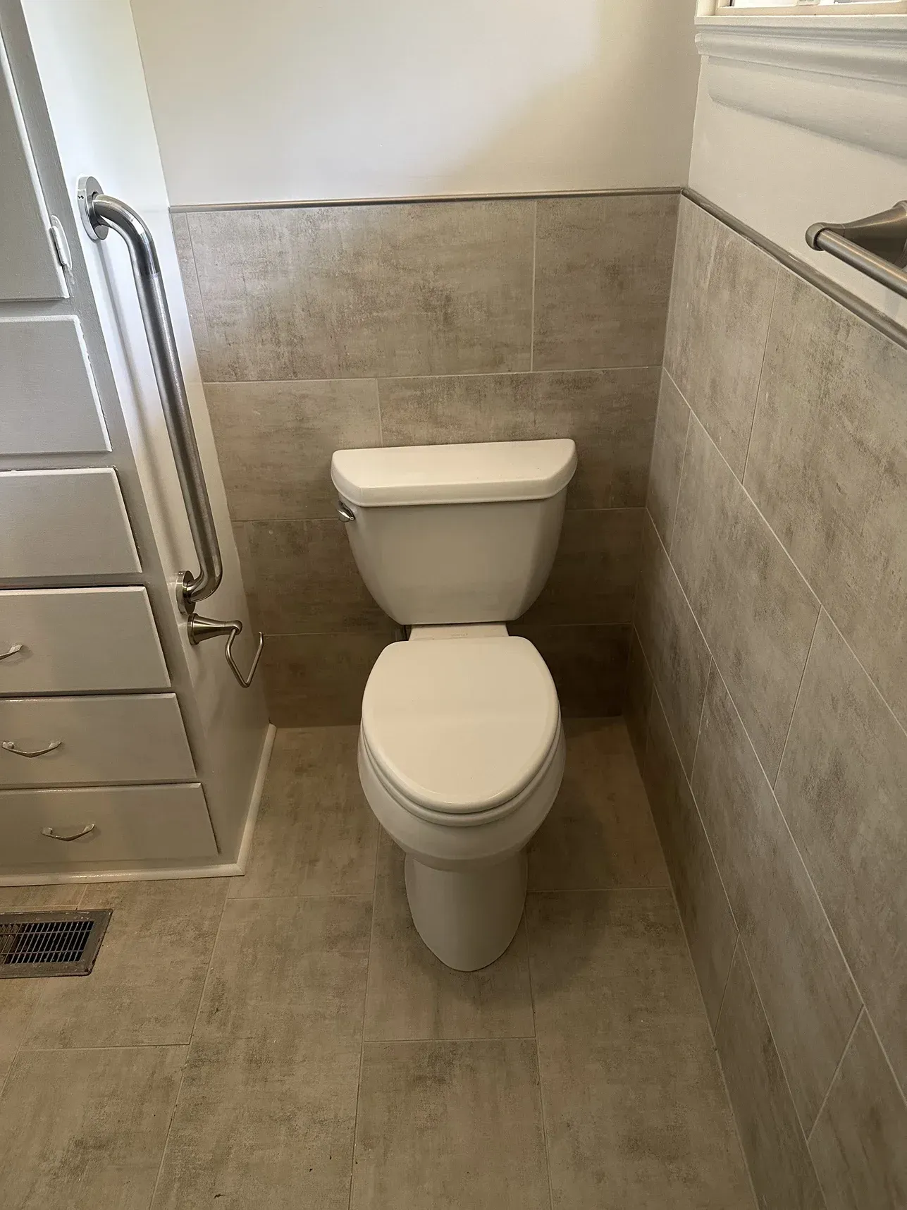Small bathroom with a white toilet, beige tile walls and floor, and grab bars beside the toilet.
