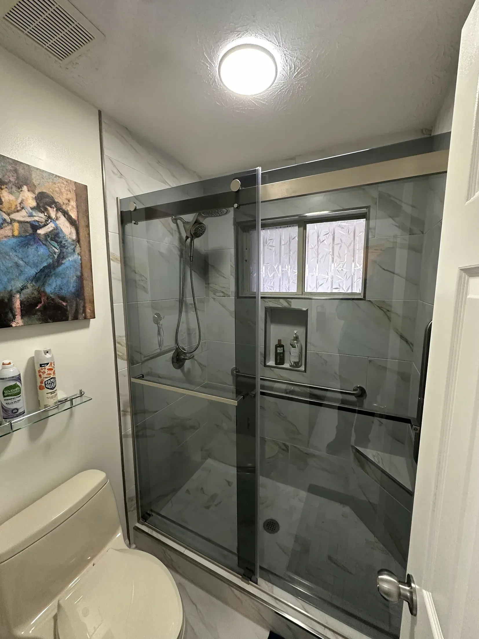 Small bathroom with a glass shower stall, toilet, wall art, and ceiling light.