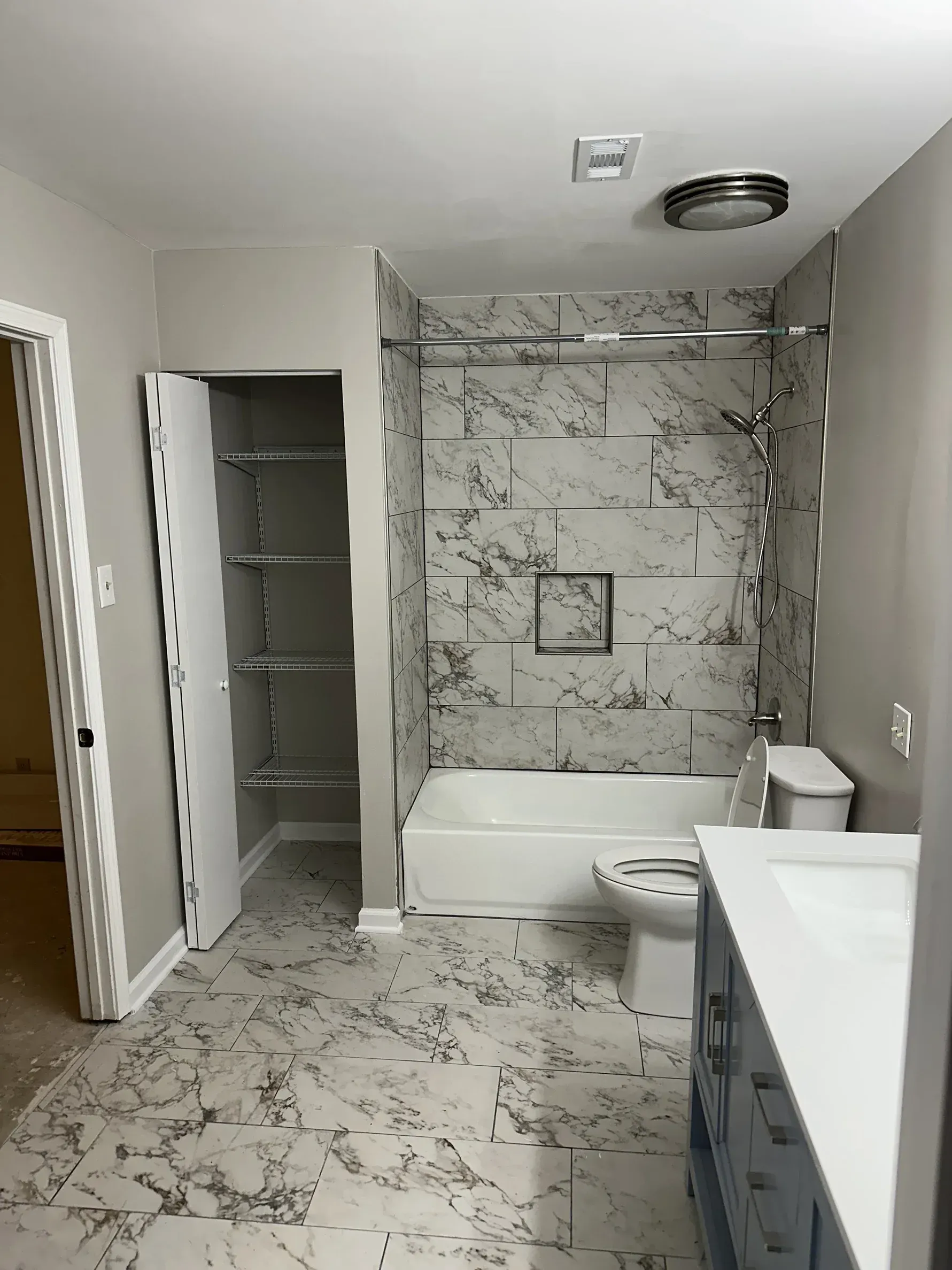 Small bathroom with marble-patterned tile, open shower, sink, and toilet.