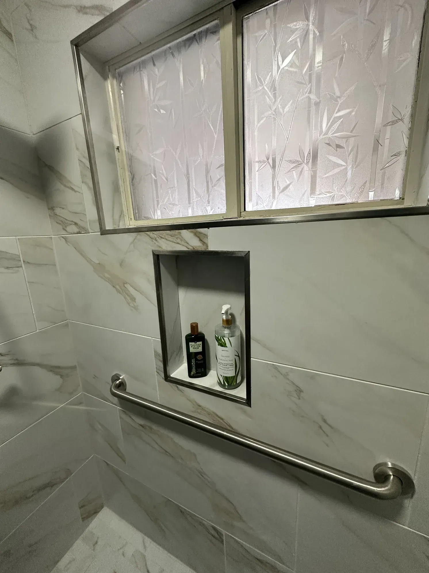 Bathroom wall mirror, shelf with toiletries, and chrome grab bar on tiled wall.