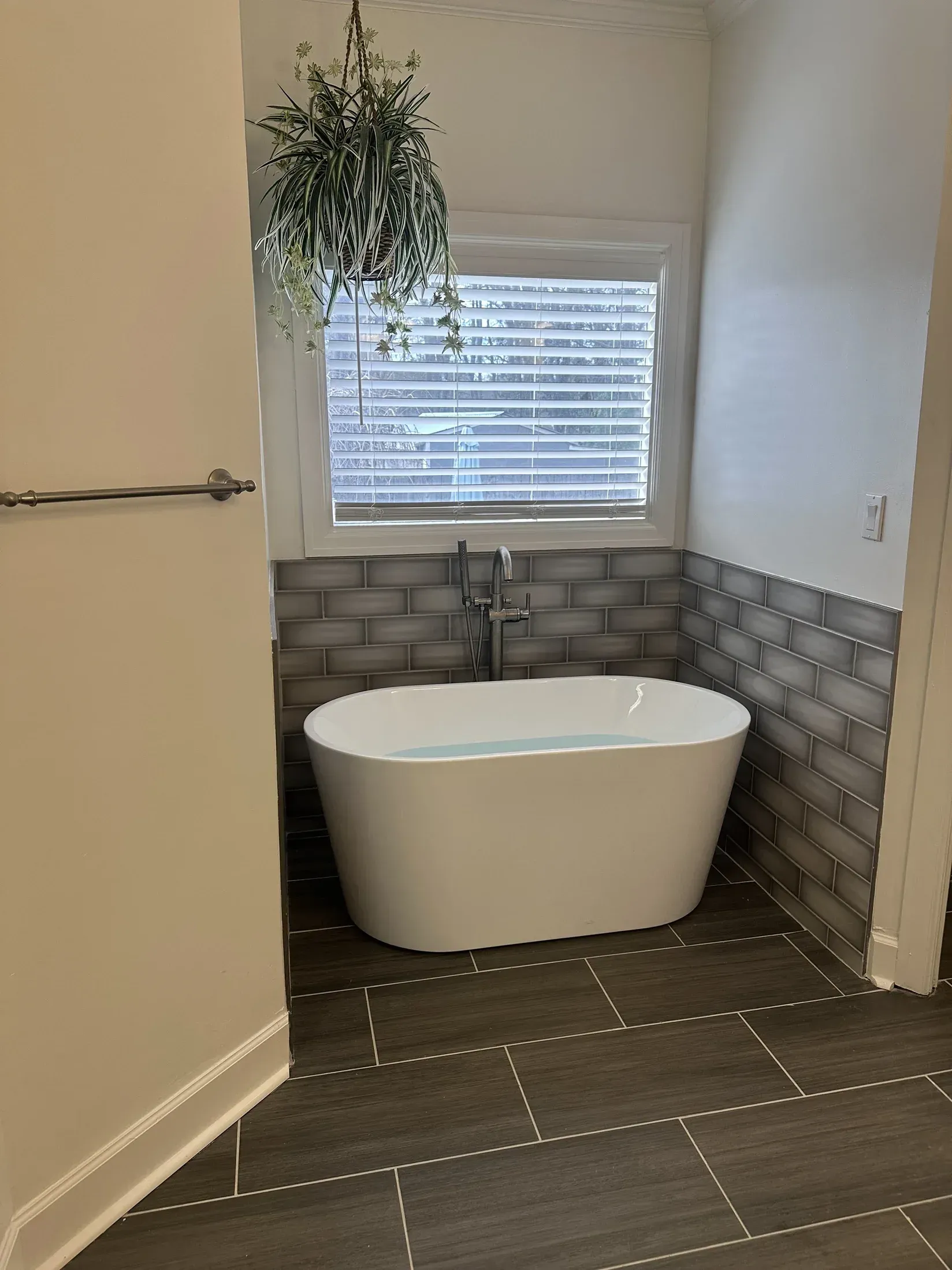 Modern bathroom with freestanding tub, window, gray tile, and hanging plant