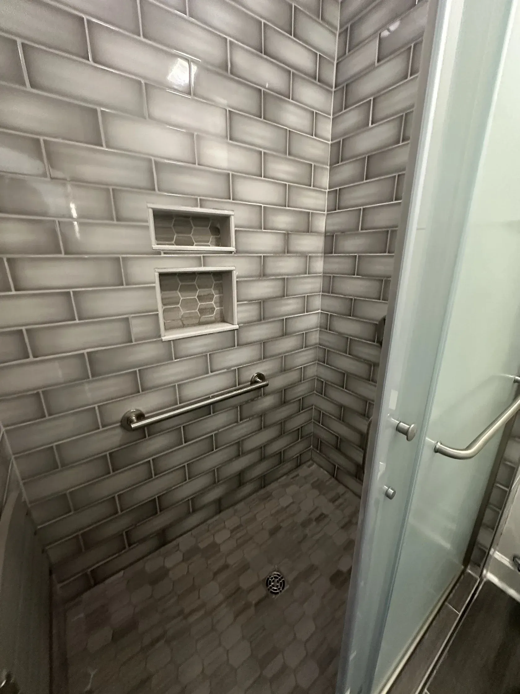 Small tiled shower stall with built-in niches and a glass door on the right.