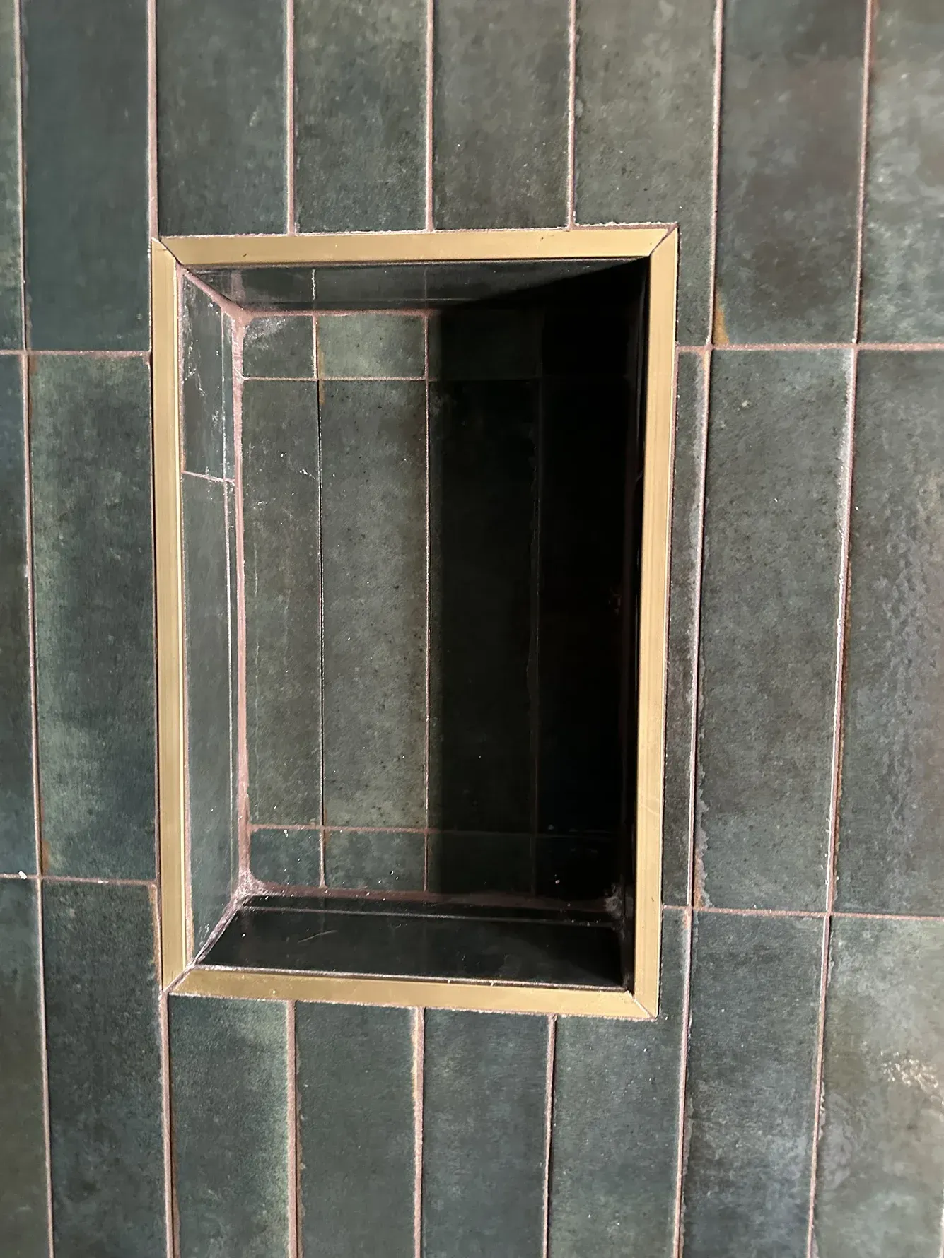 Small recessed rectangular niche with dark interior set in a green tiled wall.