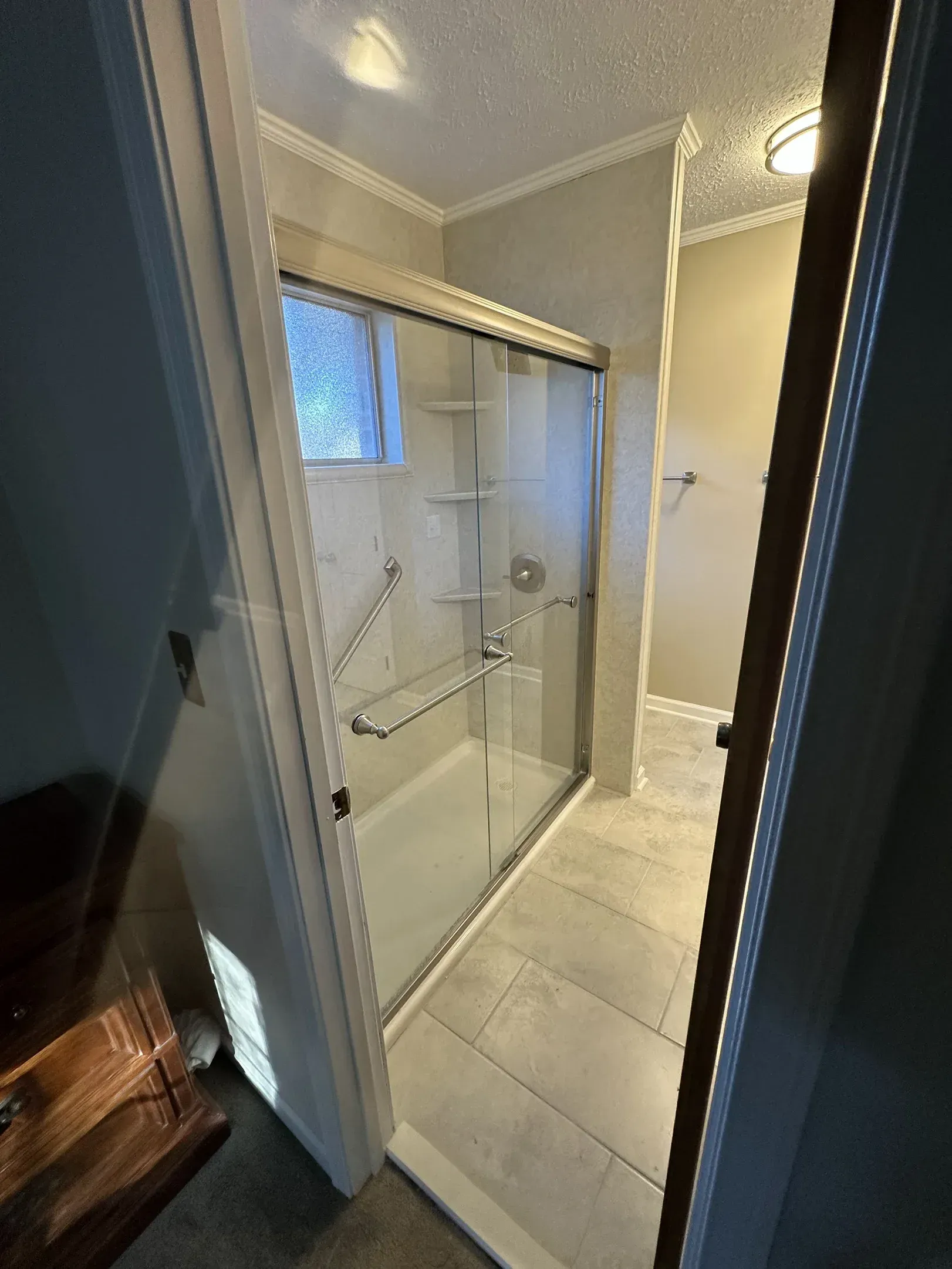 Bathroom with a glass shower enclosure, beige tile floor, and a small window above the tub area