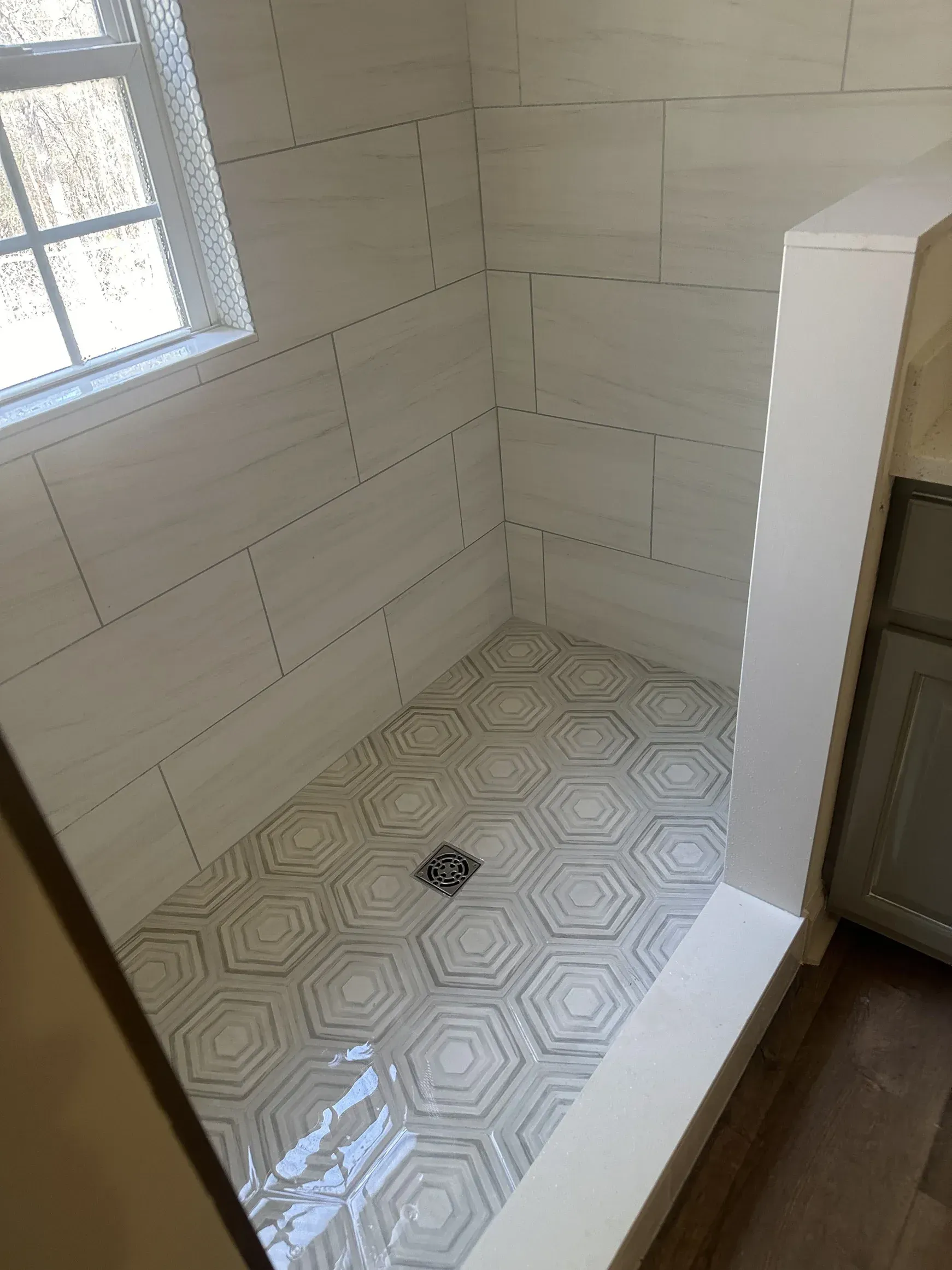 Empty tiled shower stall with a window and a floor drain