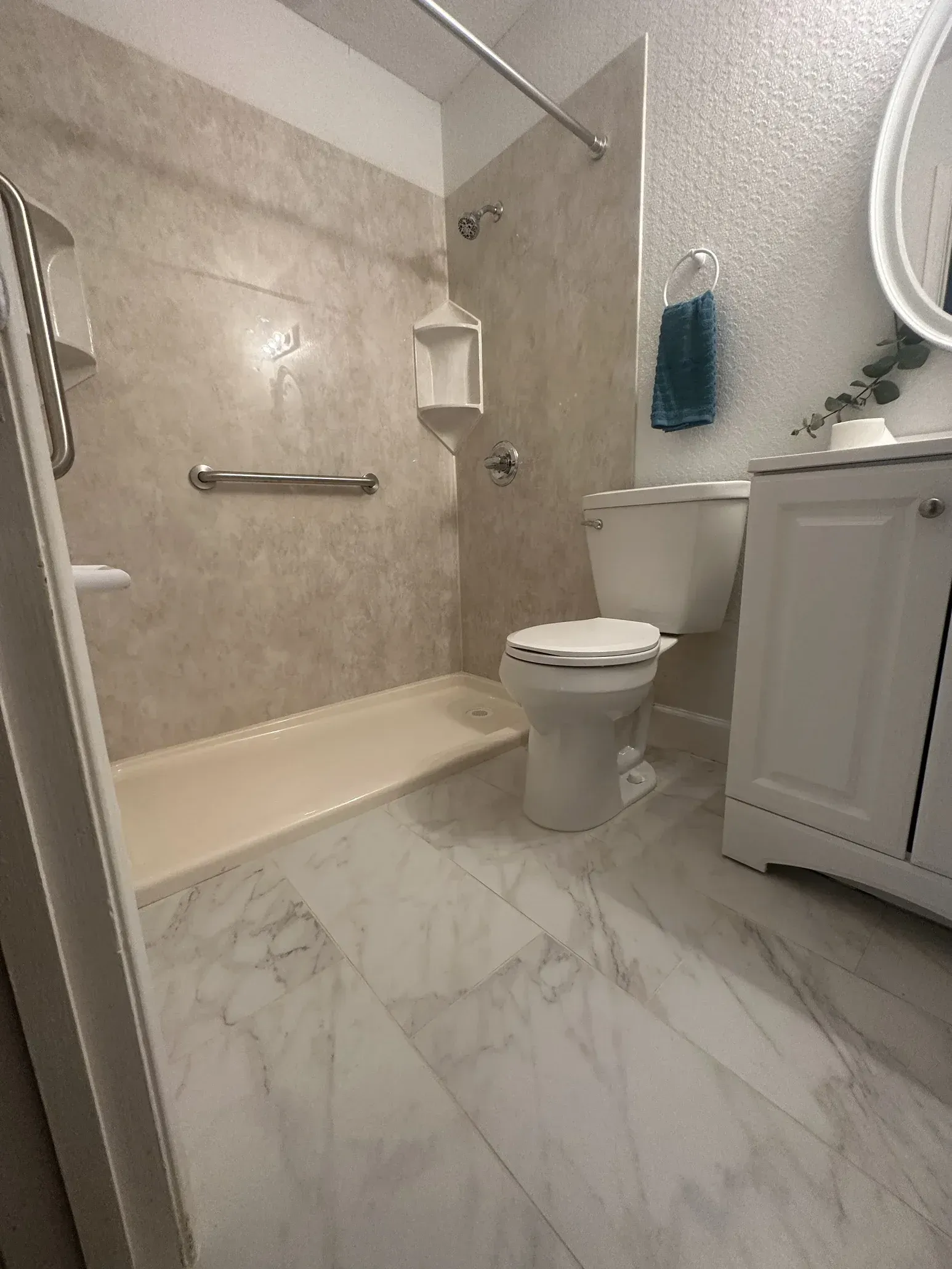 Small bathroom with beige tile, white vanity and toilet, bathtub, and marble-look floor.
