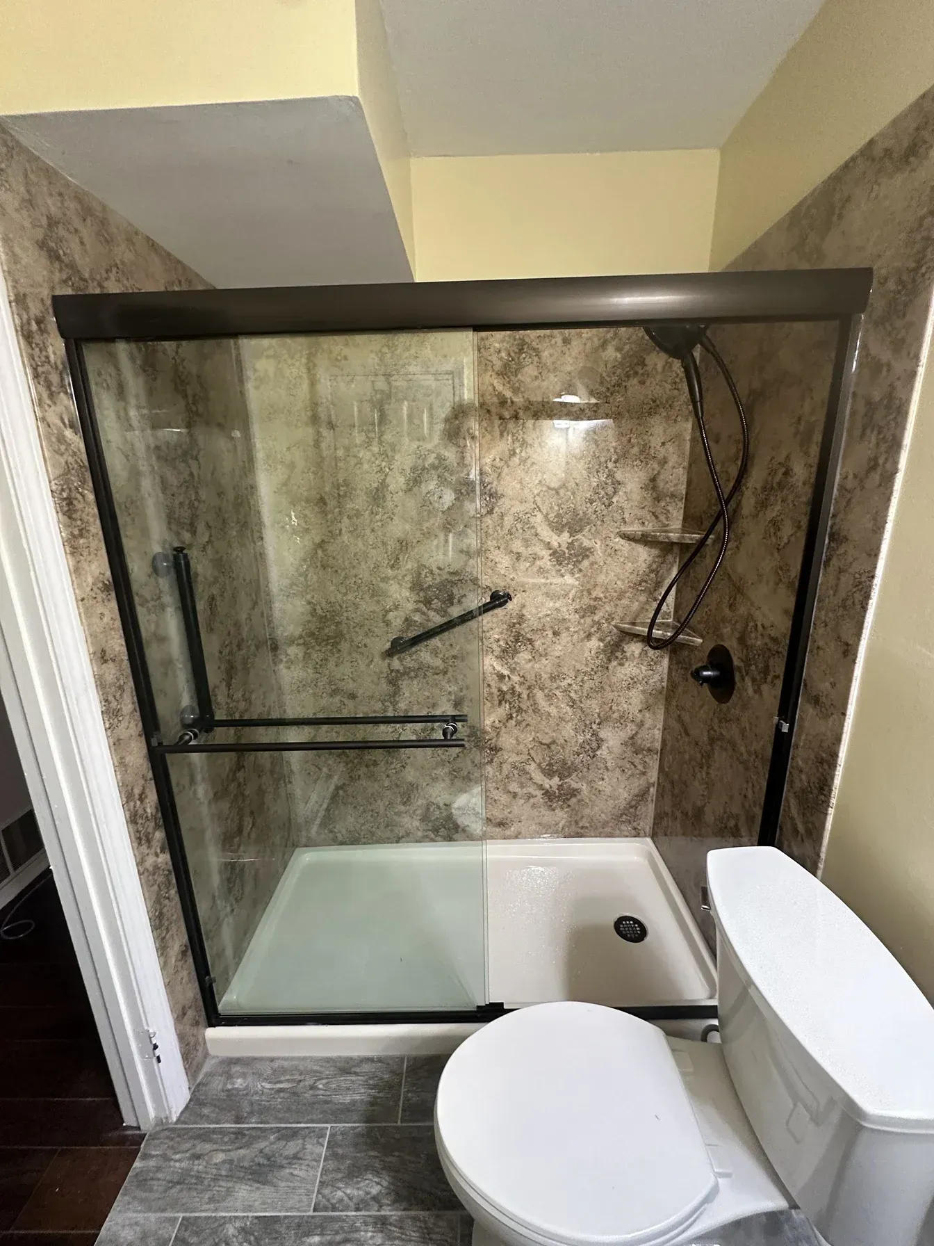 Small bathroom with a glass shower stall, white toilet, and white tub under a sloped ceiling.