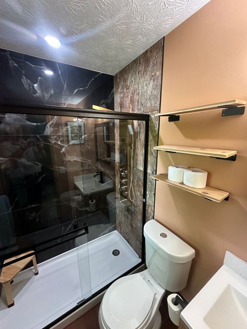 Modern bathroom with glass shower, toilet, sink, and wall shelves under warm lighting