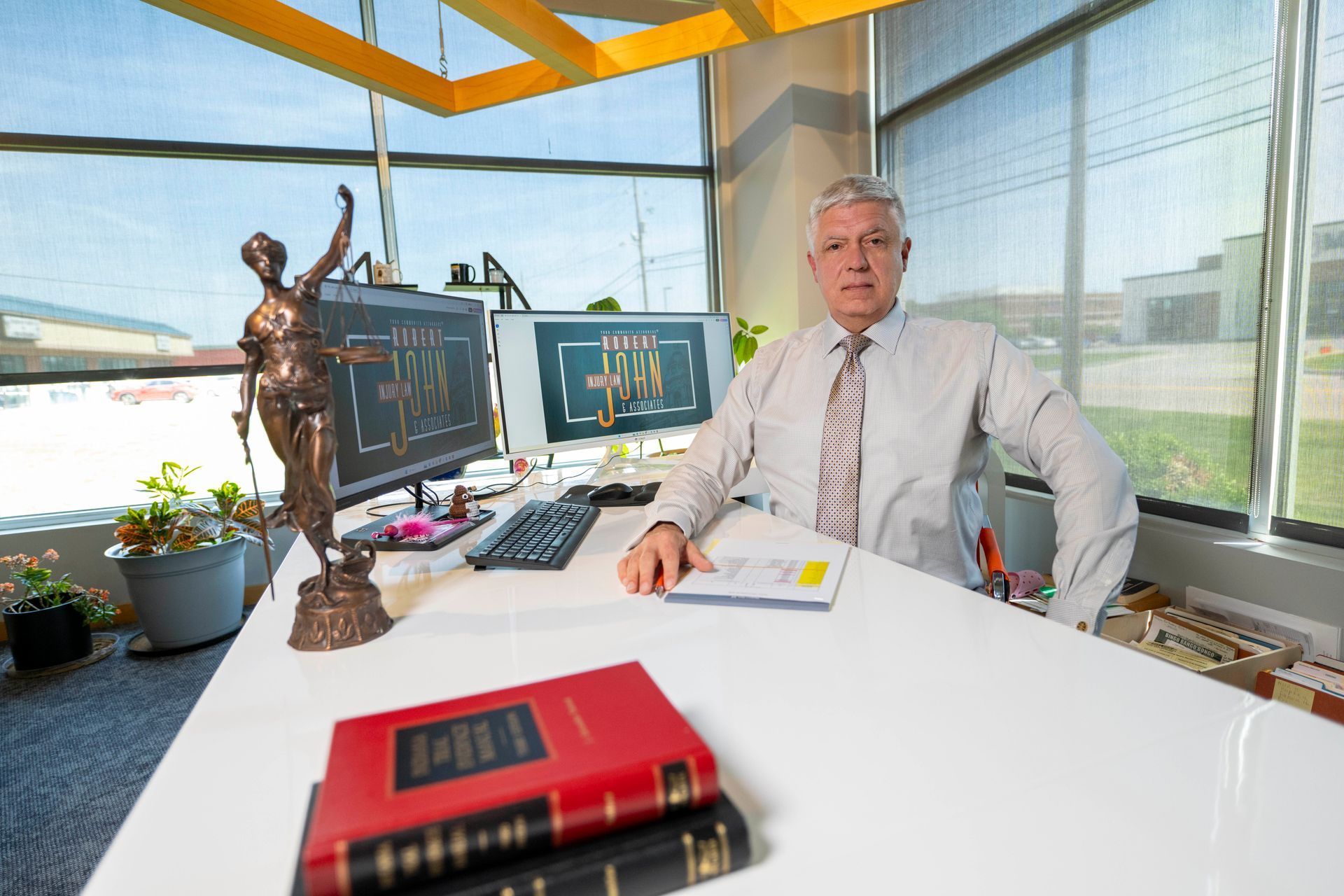 Rich Hawley seated formally in his office with law books and Lady Justice nearby.