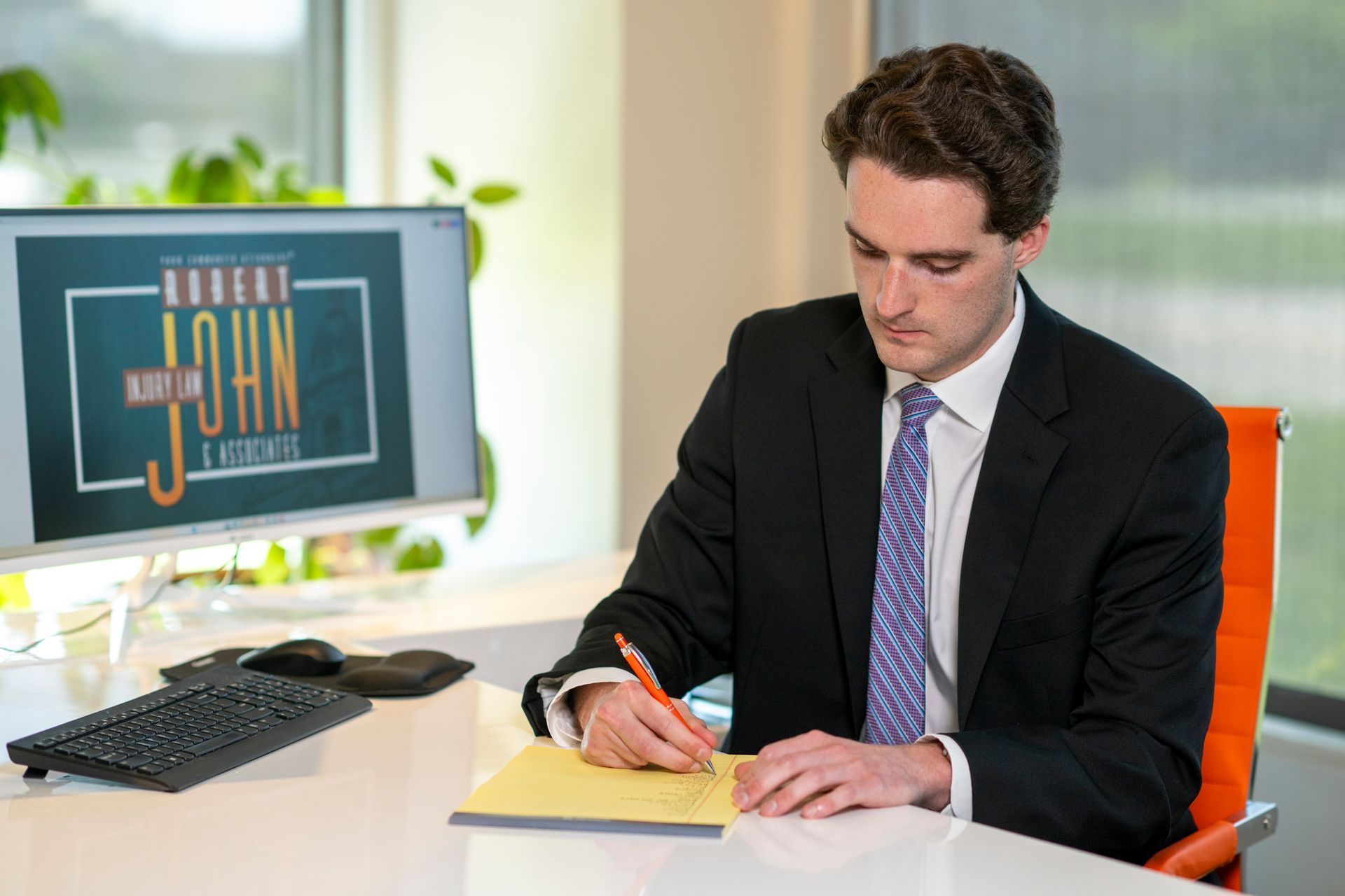 Will Marshall seated at a desk writing notes with firm branding nearby.