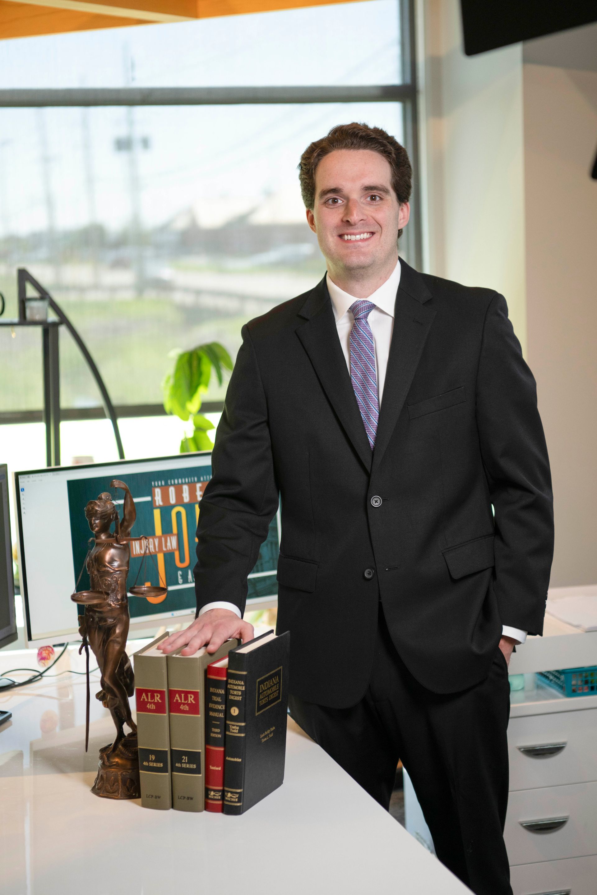 Man in a black suit standing beside a display of books in a bright office