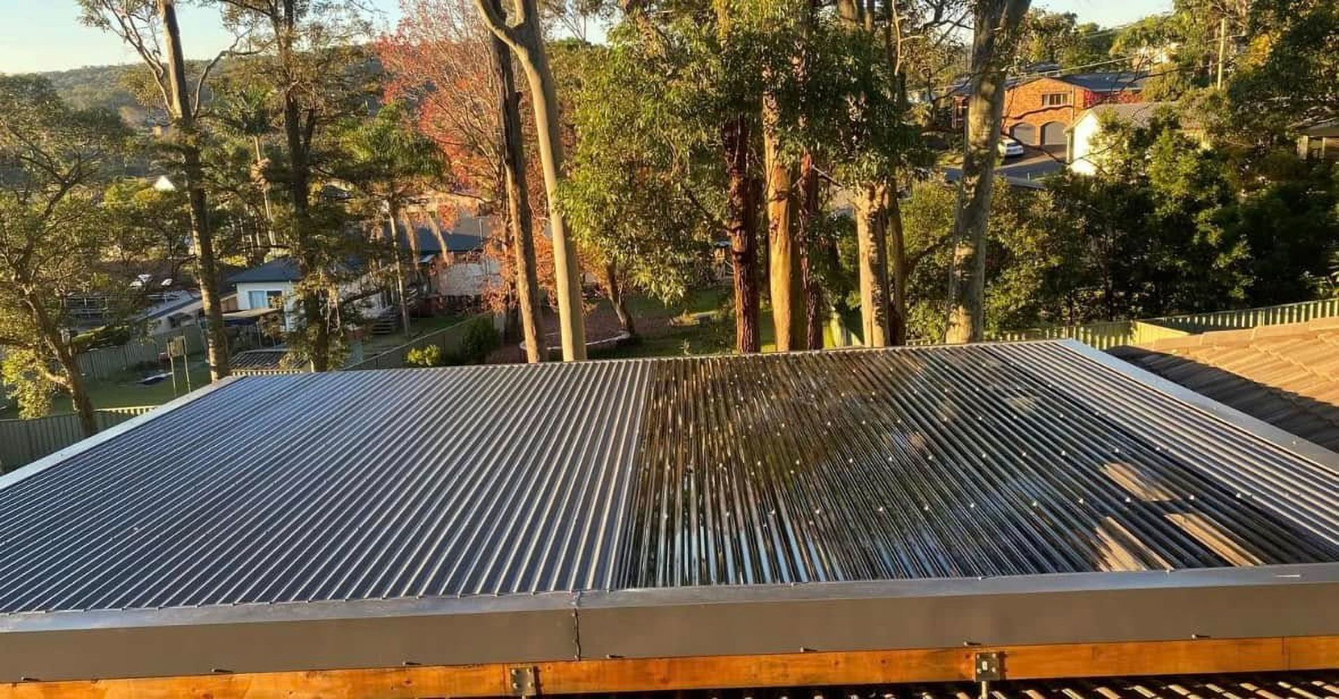 Corrugated Metal Roof, Reflecting Light, With Trees and Houses in the Background — Your Craftsmen in Newcastle, NSW