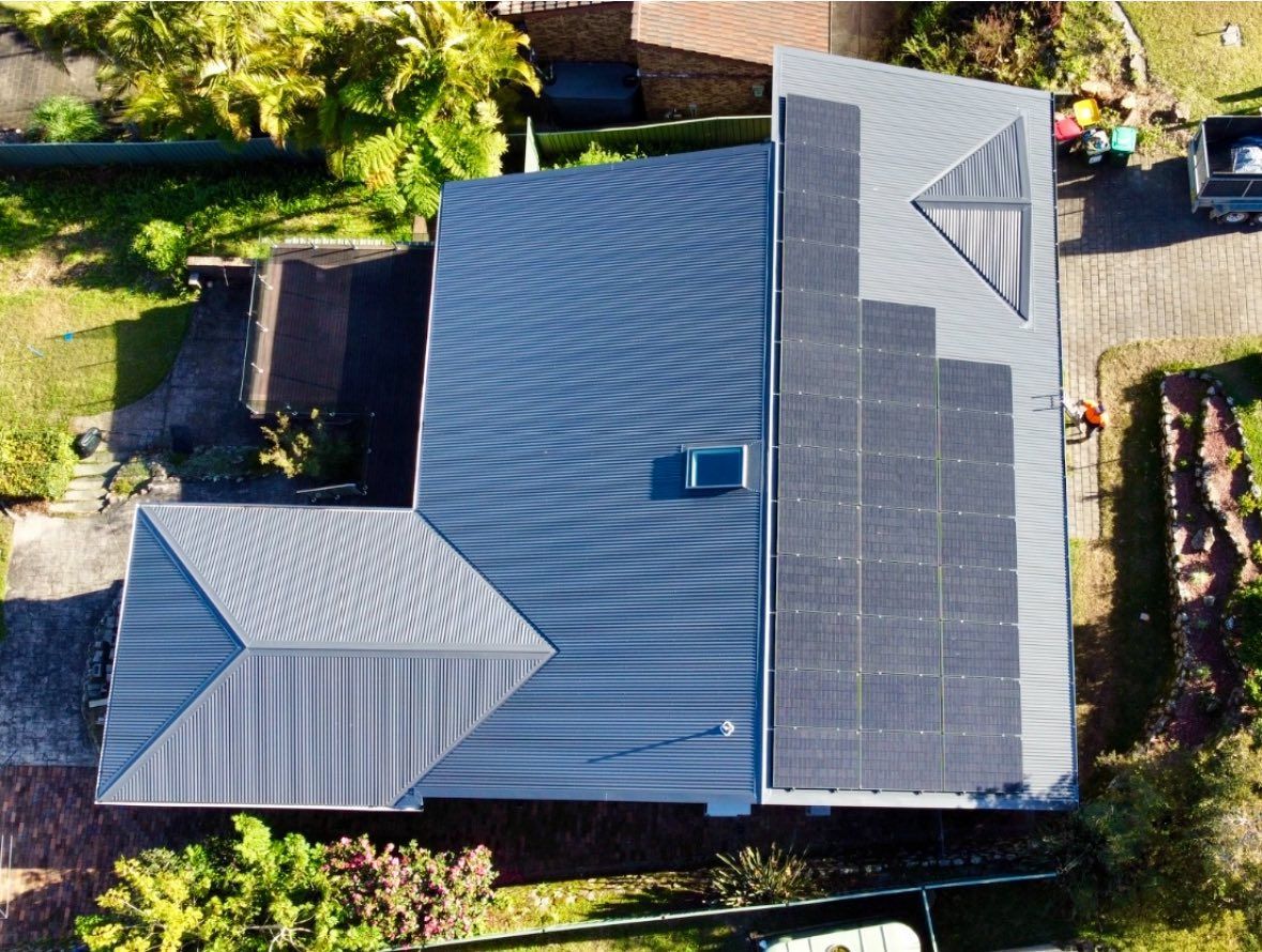 Aerial view of a gray roof with solar panels installed. The roof is surrounded by greenery, a brick driveway, and a parked vehicle. — Your Craftsmen in Eleebana, NSW