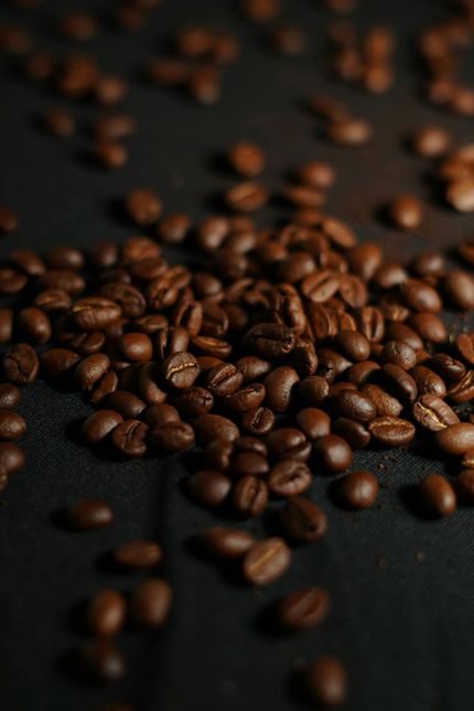 Scattered roasted coffee beans on a dark surface, with a small pile in the foreground