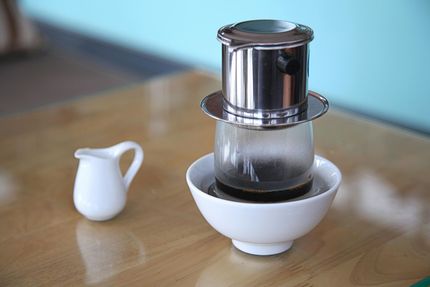 Top view of a white coffee cup with dark coffee on a gray saucer beside a glass coffee pot.