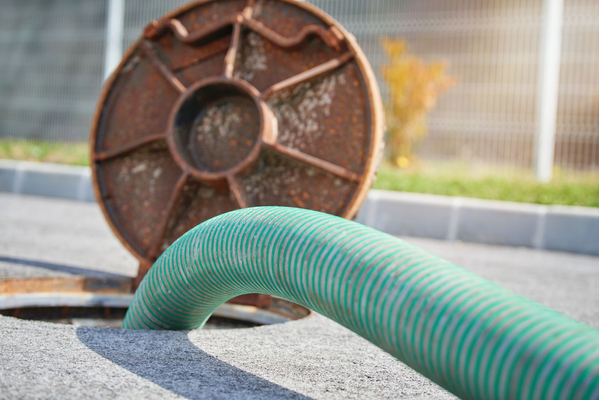 Green corrugated pipe emerging from gravel near a rusted wheel in an outdoor industrial setting