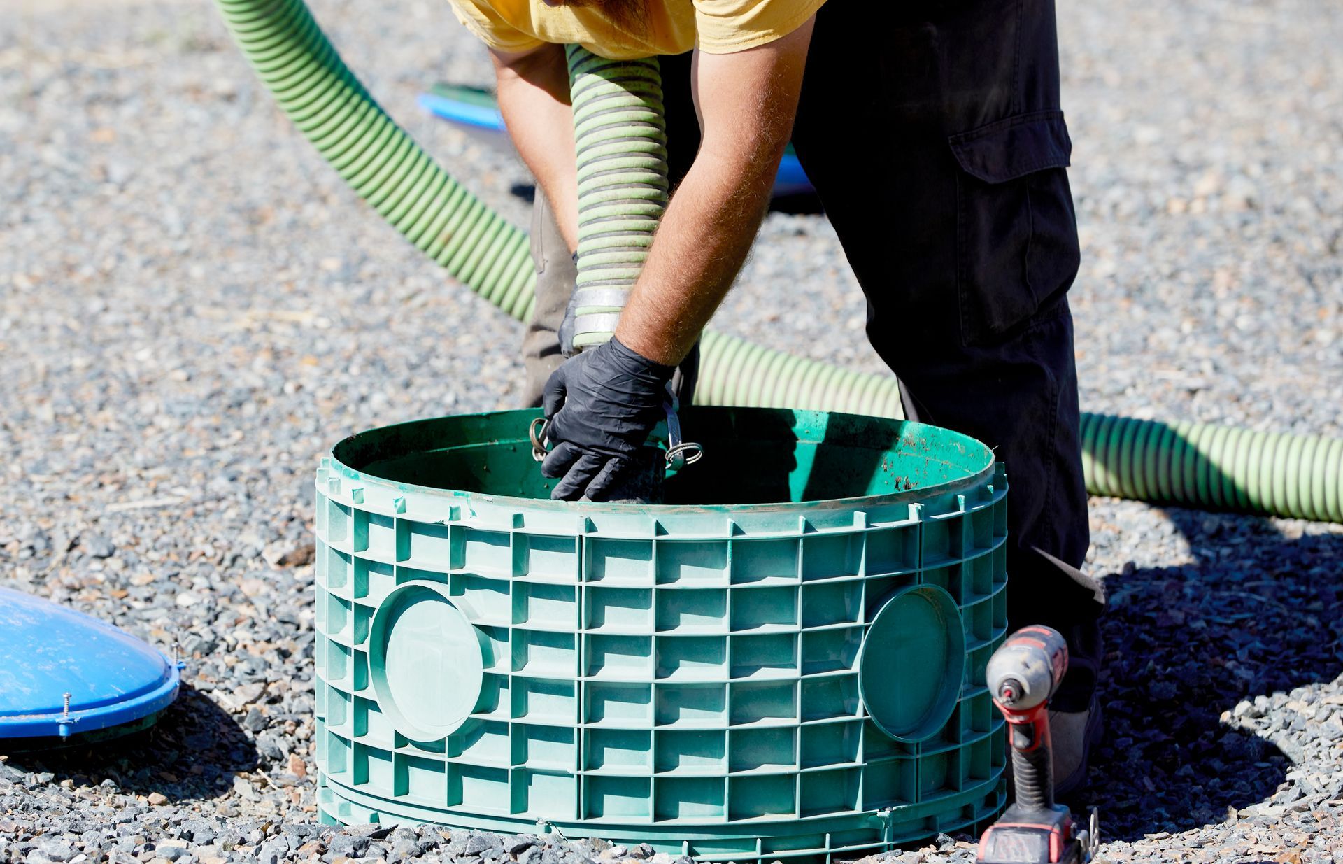 Worker in gloves installing a green plastic utility box with hose attached outdoors